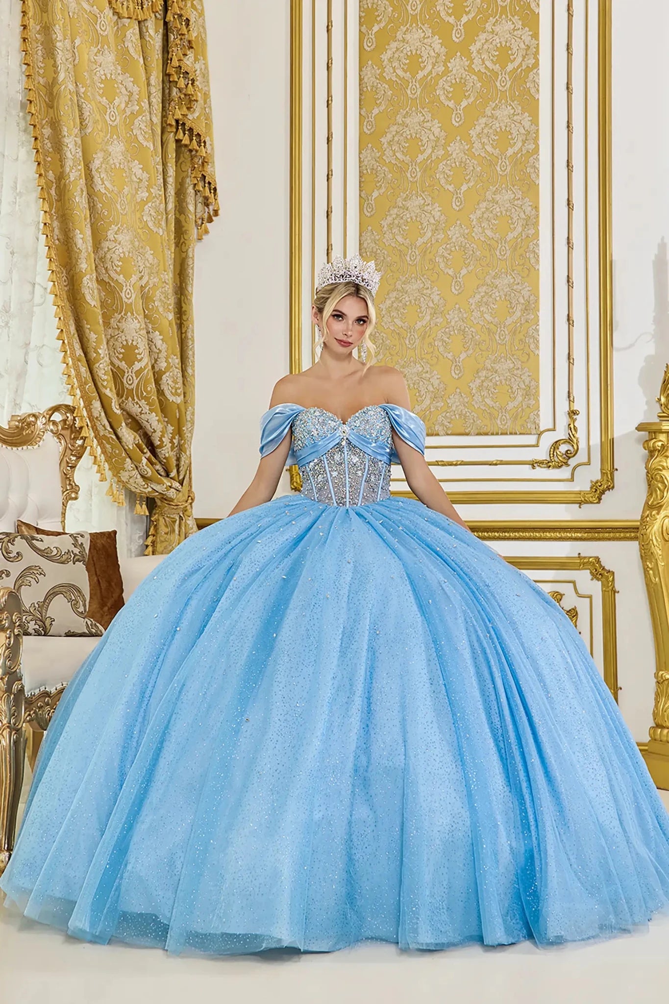 Off-the-shoulder light blue quinceañera ball gown with crystal-embellished corset bodice and full glitter tulle skirt in an elegant gold-accented interior