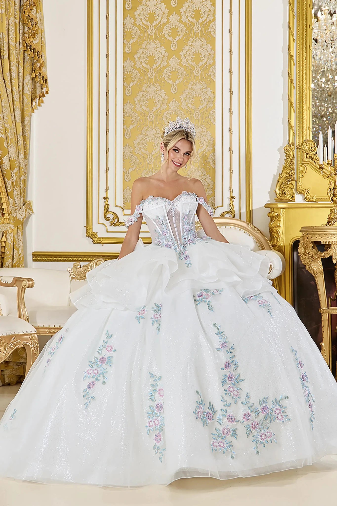 Woman in Off white off-shoulder quinceañera ball gown with floral corset and glitter tulle skirt.