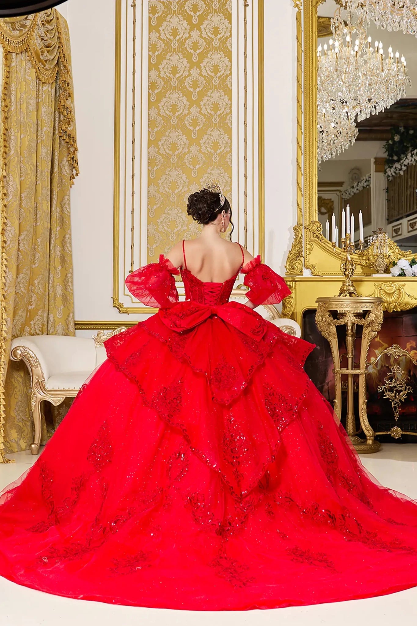 Woman standing back-facing in red ball gown with lace-up closure, detachable puff sleeves, beaded bodice accents, and cascading tulle skirt