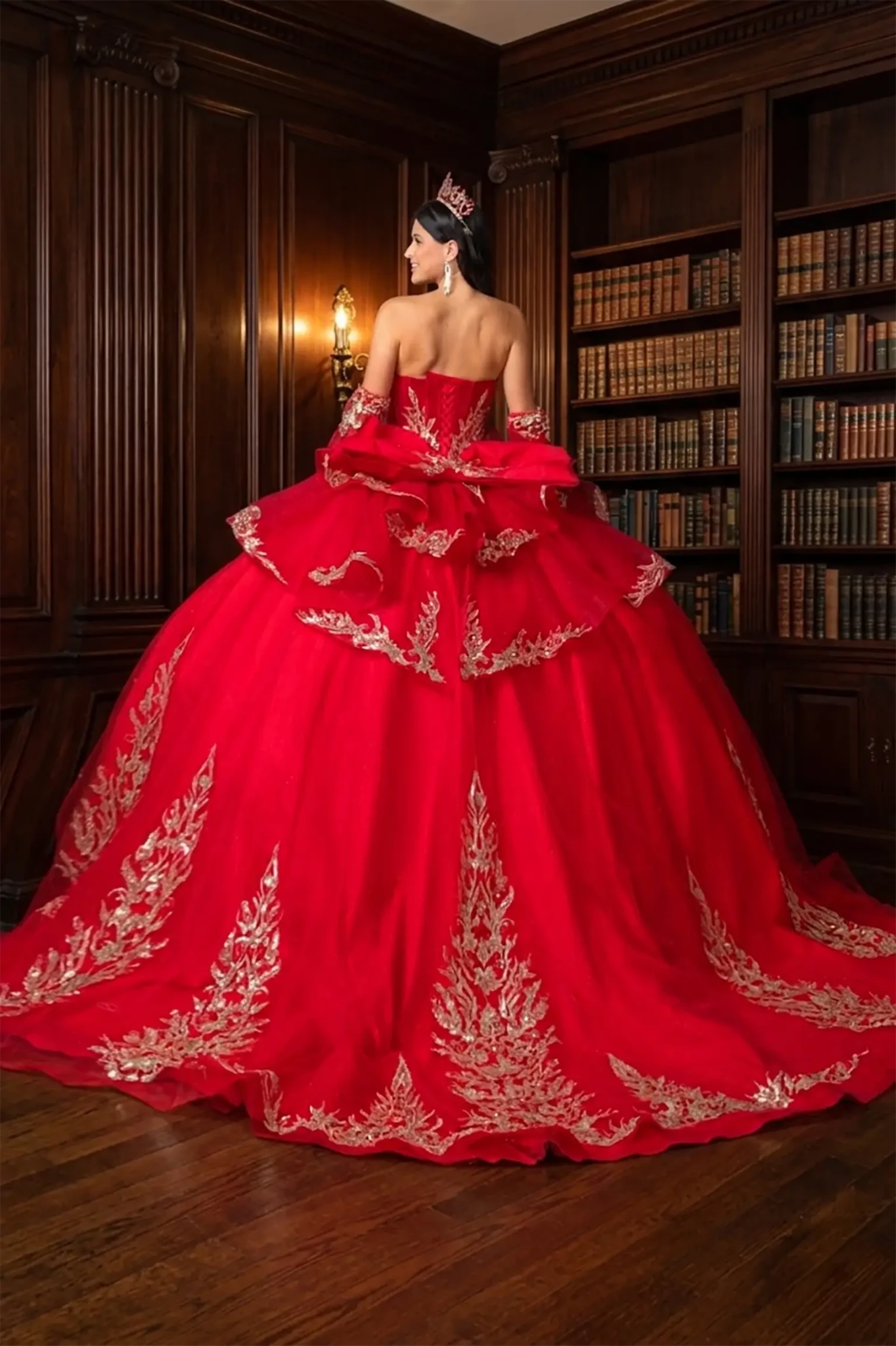 woman back-facing in red off-shoulder ball gown quinceañera dress with long train and big bow