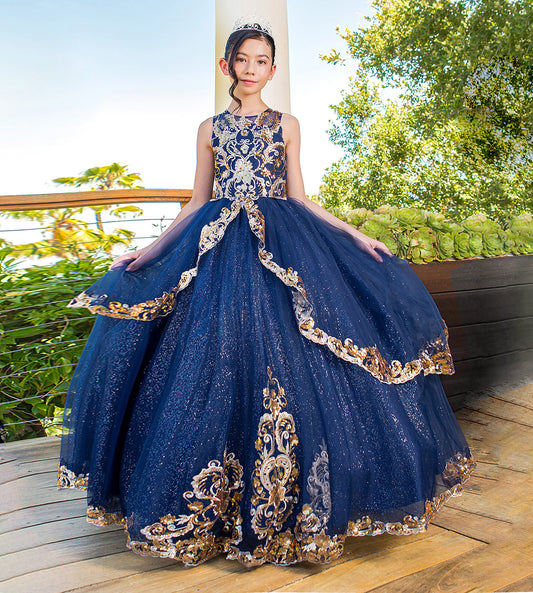 Girl in a blue and gold evening gown standing outdoors with trees in the background