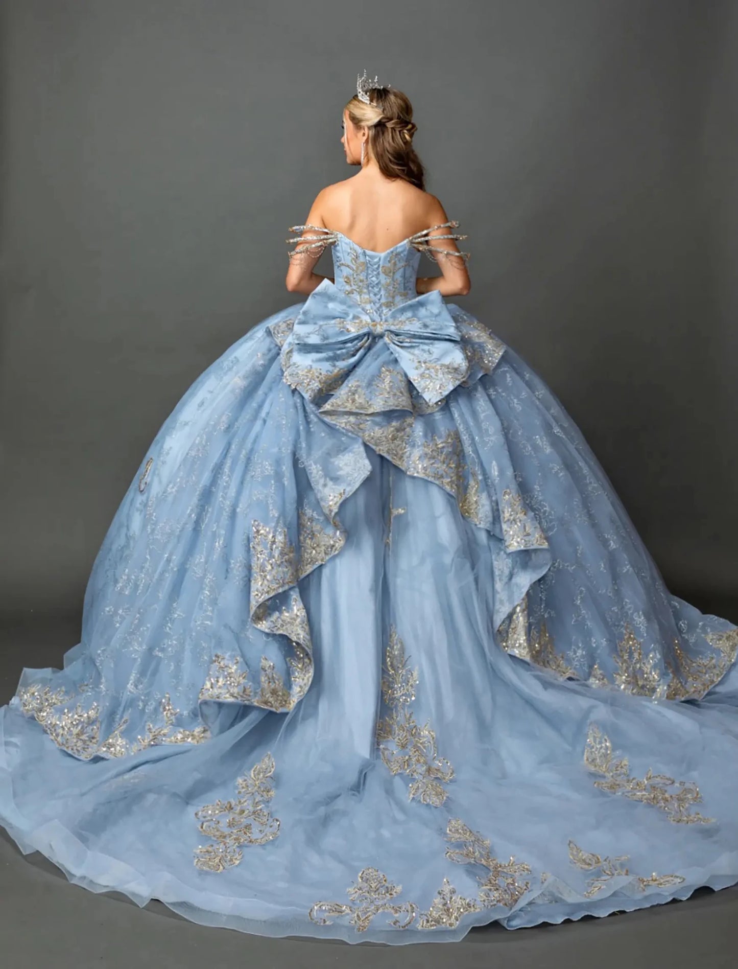 Back view of a woman wearing dusty blue quinceañera, lace-up, glitter tulle, metallic embroidery, off-shoulder sleeves