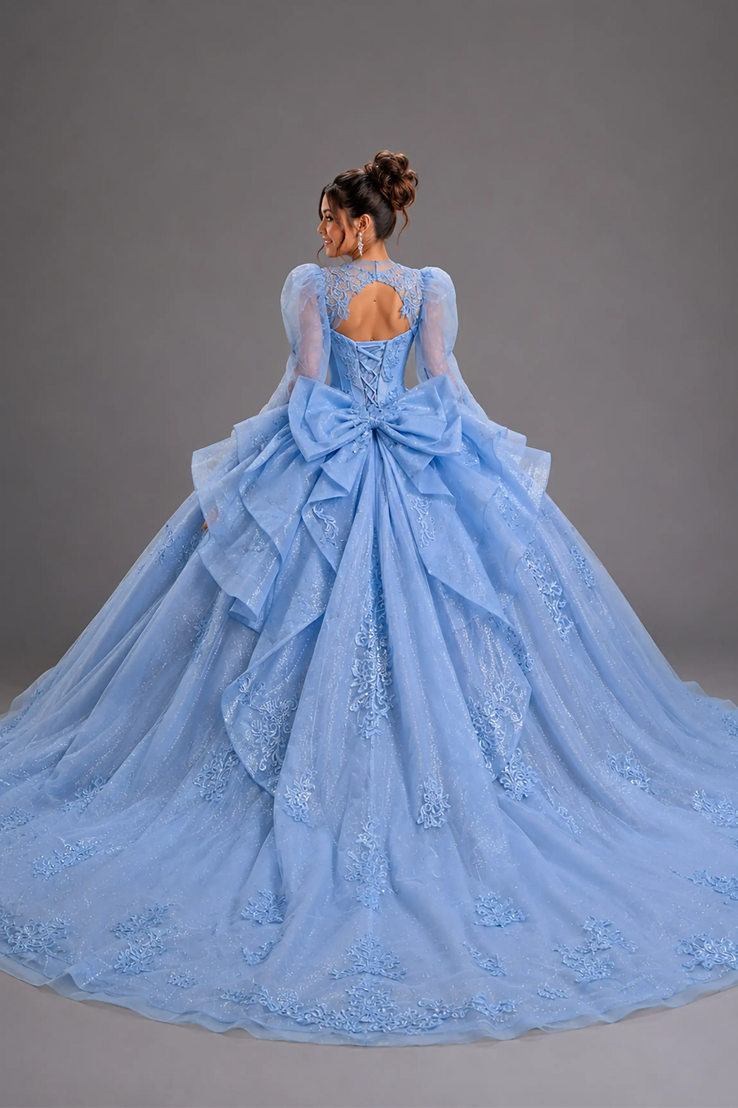 Back view of a woman wearing bahama blue quinceañera dress featuring corset back design, tiered ruffle skirt, and glitter tulle