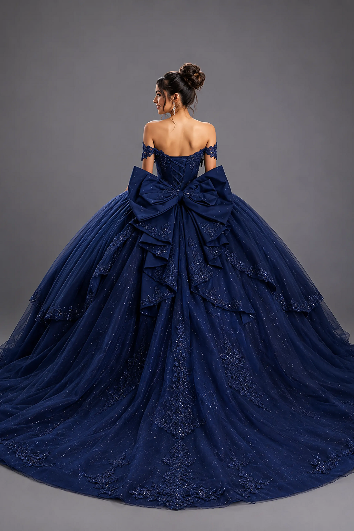 Back view of a woman wearing navy quinceañera dress featuring large bow detail, lace-up corset back, and layered glitter tulle skirt