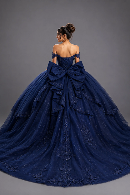 Back view of a woman wearing navy quinceañera dress featuring large bow detail, lace-up corset back, and layered glitter tulle skirt