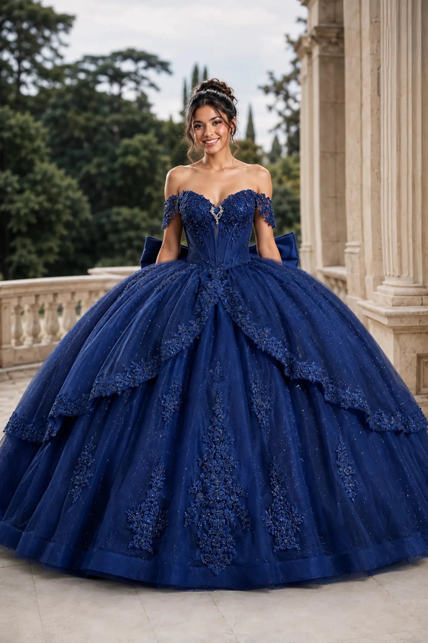 Front view of a woman wearing navy quinceañera dress featuring floral embroidery, tiered overskirt, corset bodice, and glitter tulle