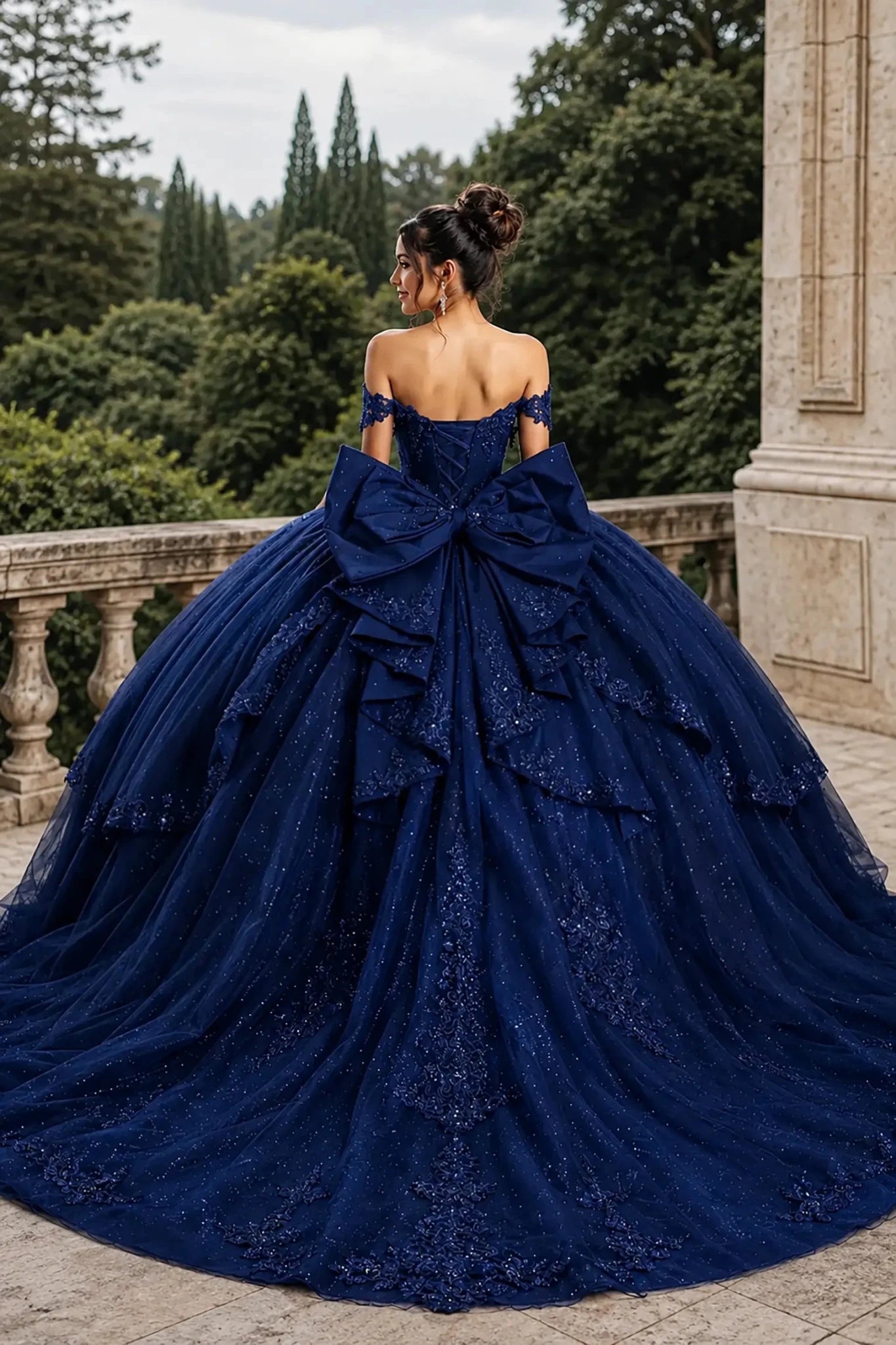Back view of a woman wearing navy quinceañera dress featuring large bow detail, lace-up corset back, and layered glitter tulle skirt