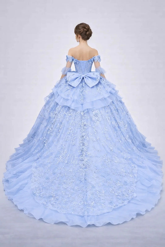 Woman standing back-facing in Bahama blue ball gown with lace-up closure, floral appliqué accents, glitter tulle layers, and cascading skirt