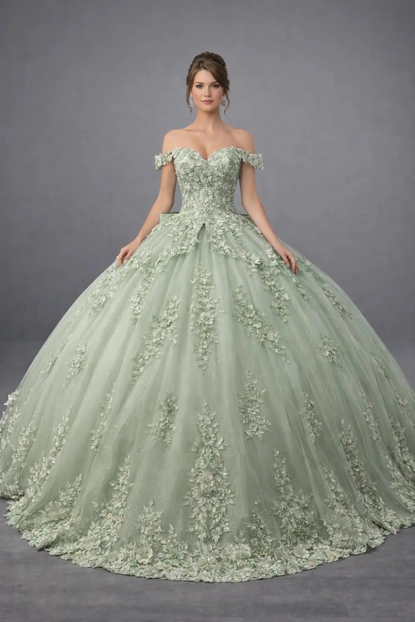 Woman standing front-facing in elegant sage ball gown with 3D floral appliqué bodice, ruffle sleeves, and voluminous layered skirt