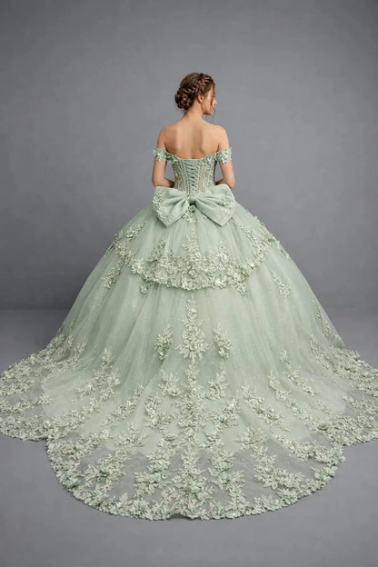 Woman standing back-facing in sage ball gown with lace-up closure, 3D floral appliqué accents, ruffle sleeves, and cascading skirt