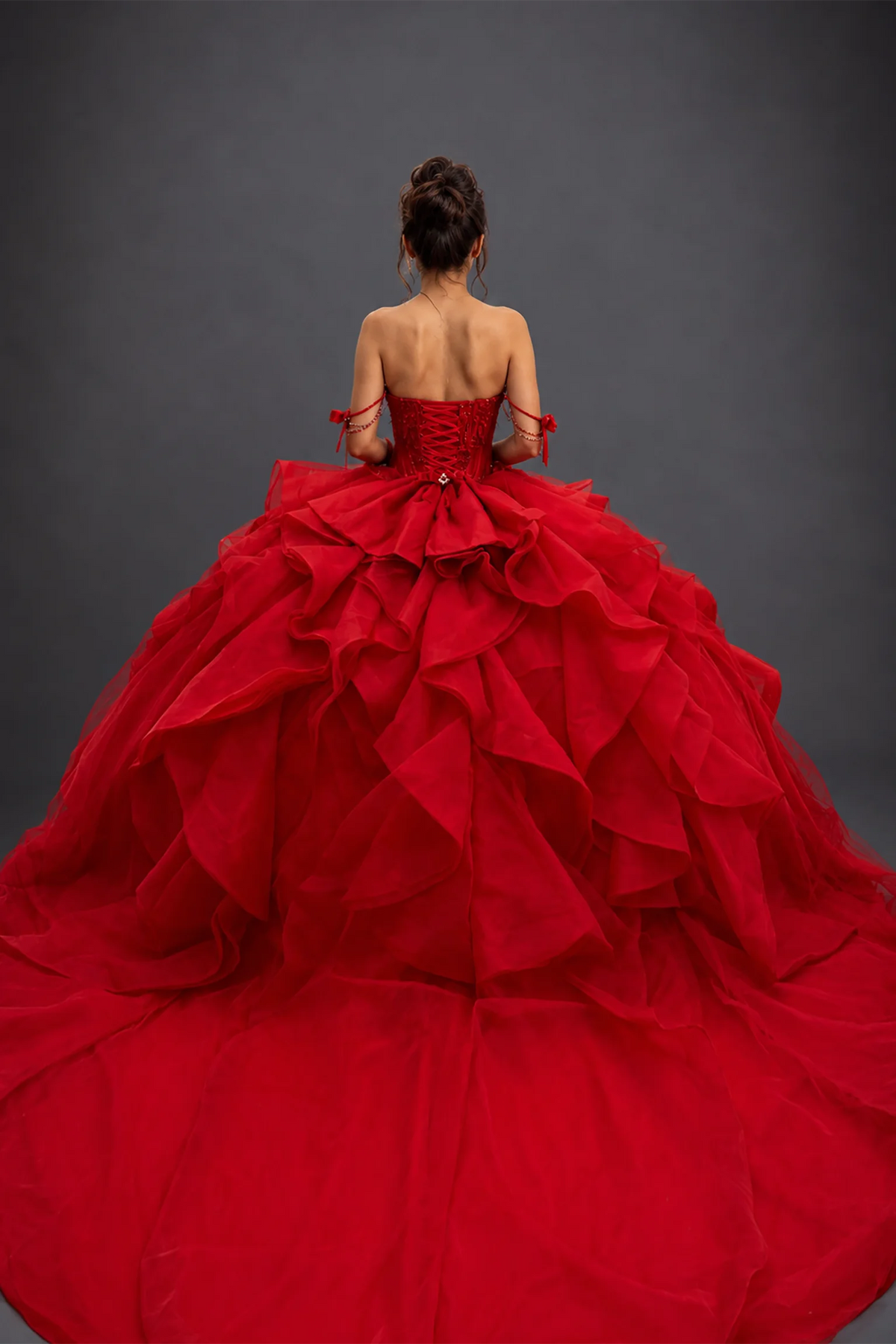 Back view of red quinceañera dress with lace-up corset and tiered ruffle train