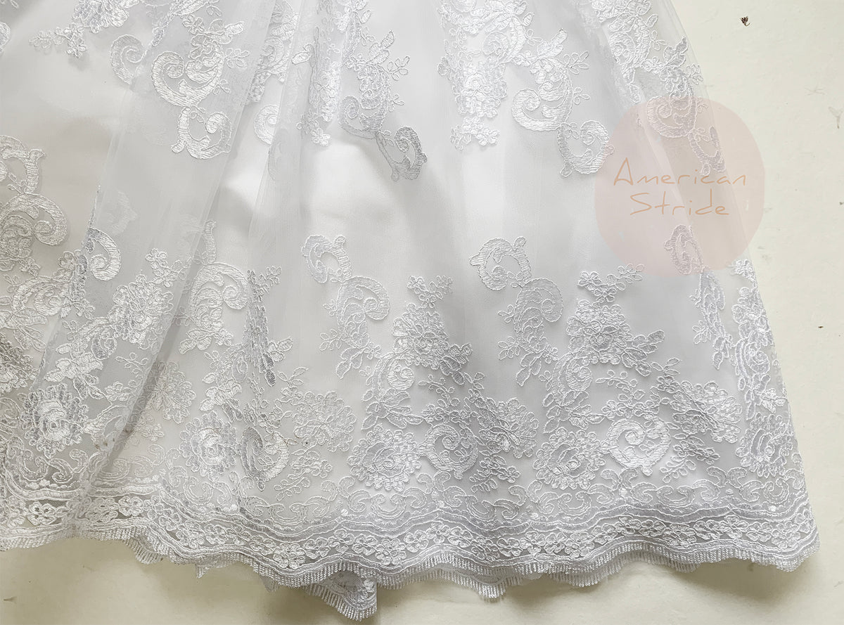 Intricate features stand out across white communion dress skirt showing layered tulle and floral lace embroidery along the hem.