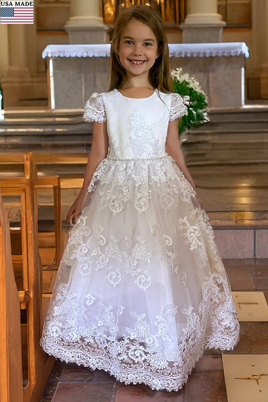 Young girl in a white lace first communion dress with cap sleeves standing in a church.