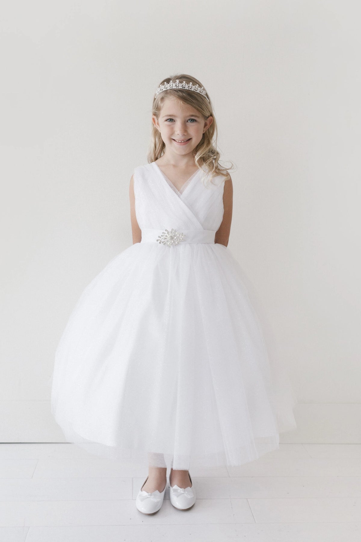 The White kids pageant dress has a ruched V-neckline and rhinestone brooch.