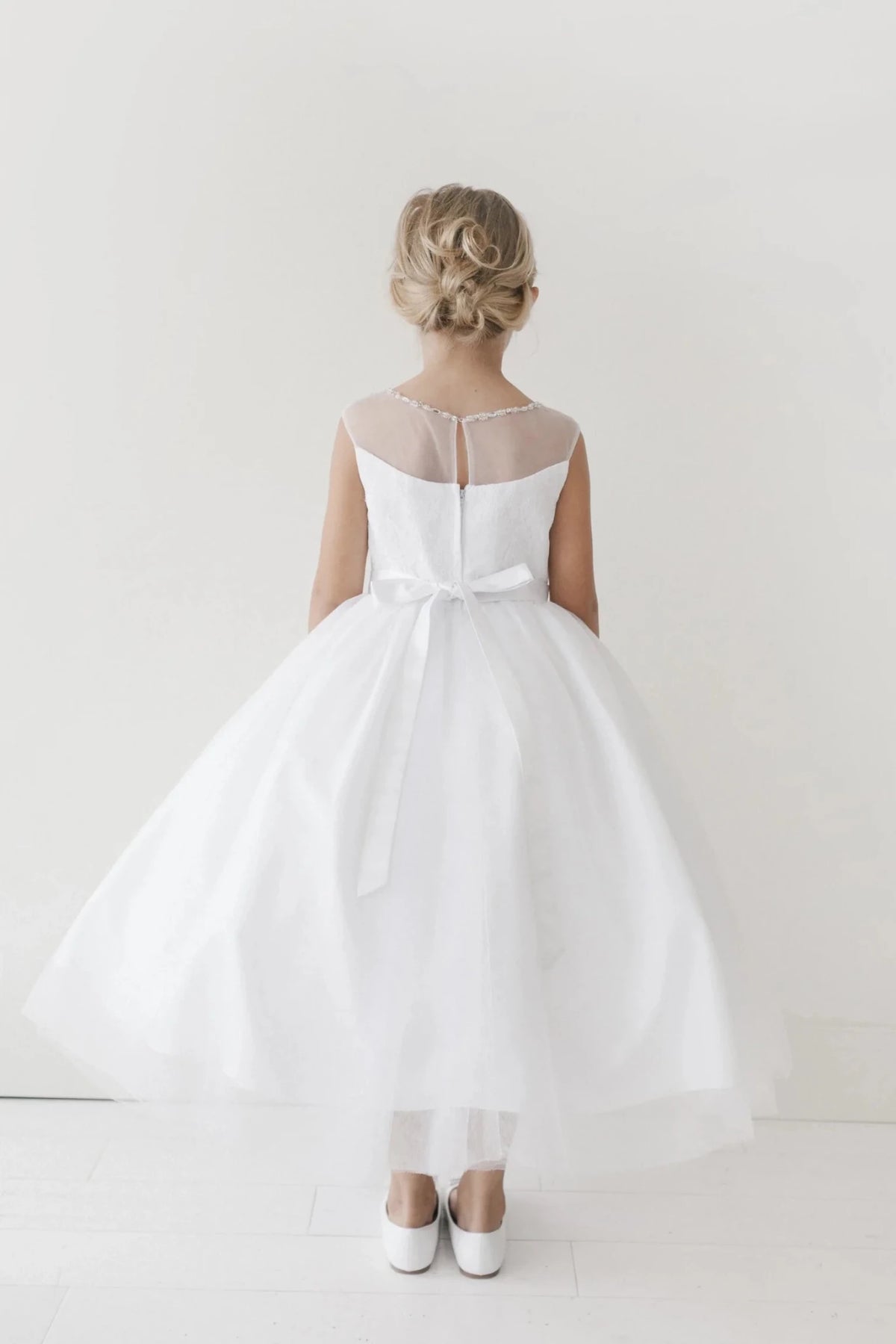 Ribbon tails fall over the off-white flower girl dress's back skirt.