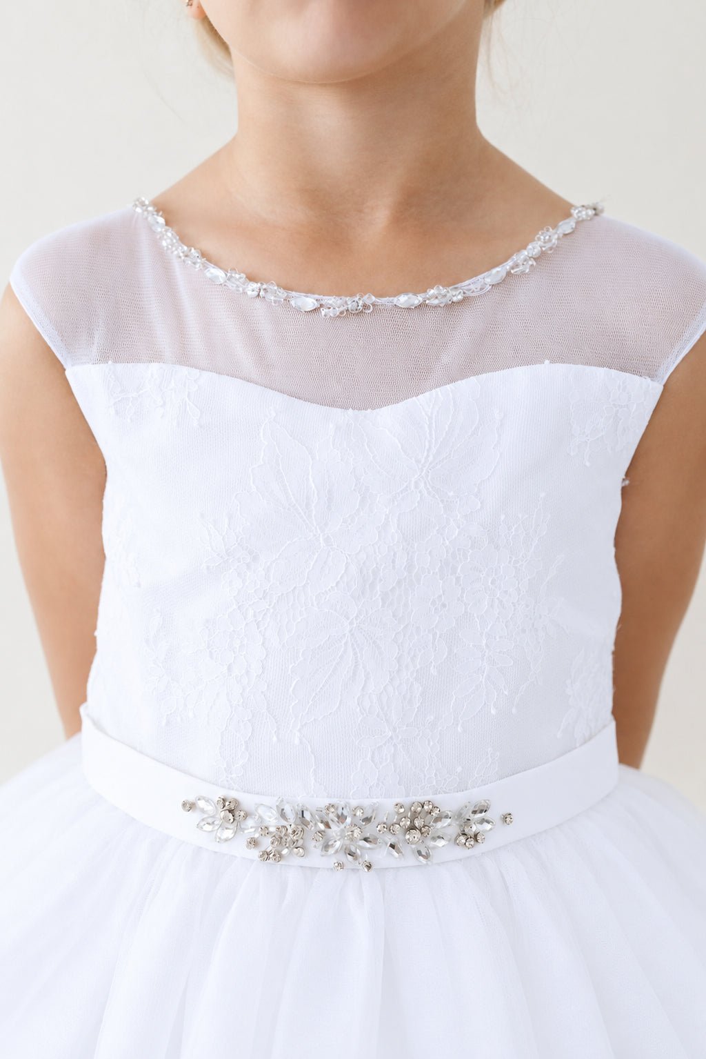 Tiny flowers texture the white flower girl dress's fitted bodice.