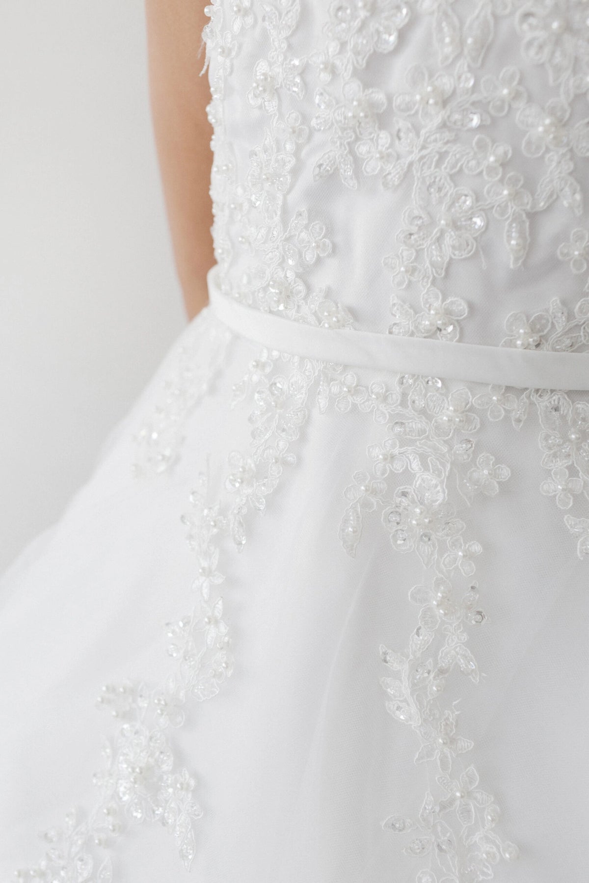 Pearl-like beads accent lace on the off-white flower girl dress's waist.
