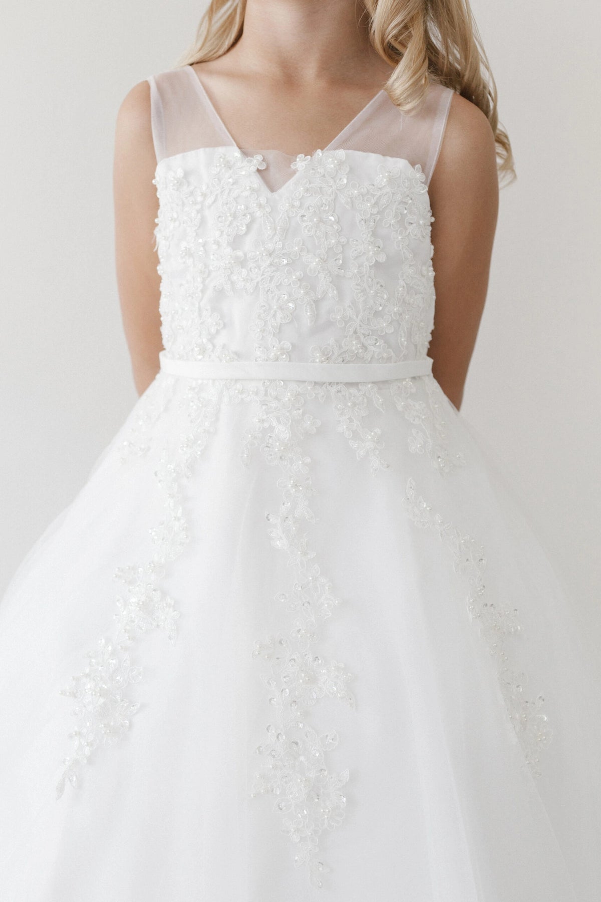 Off-white flower girl dress with delicate blossoms over its bodice.