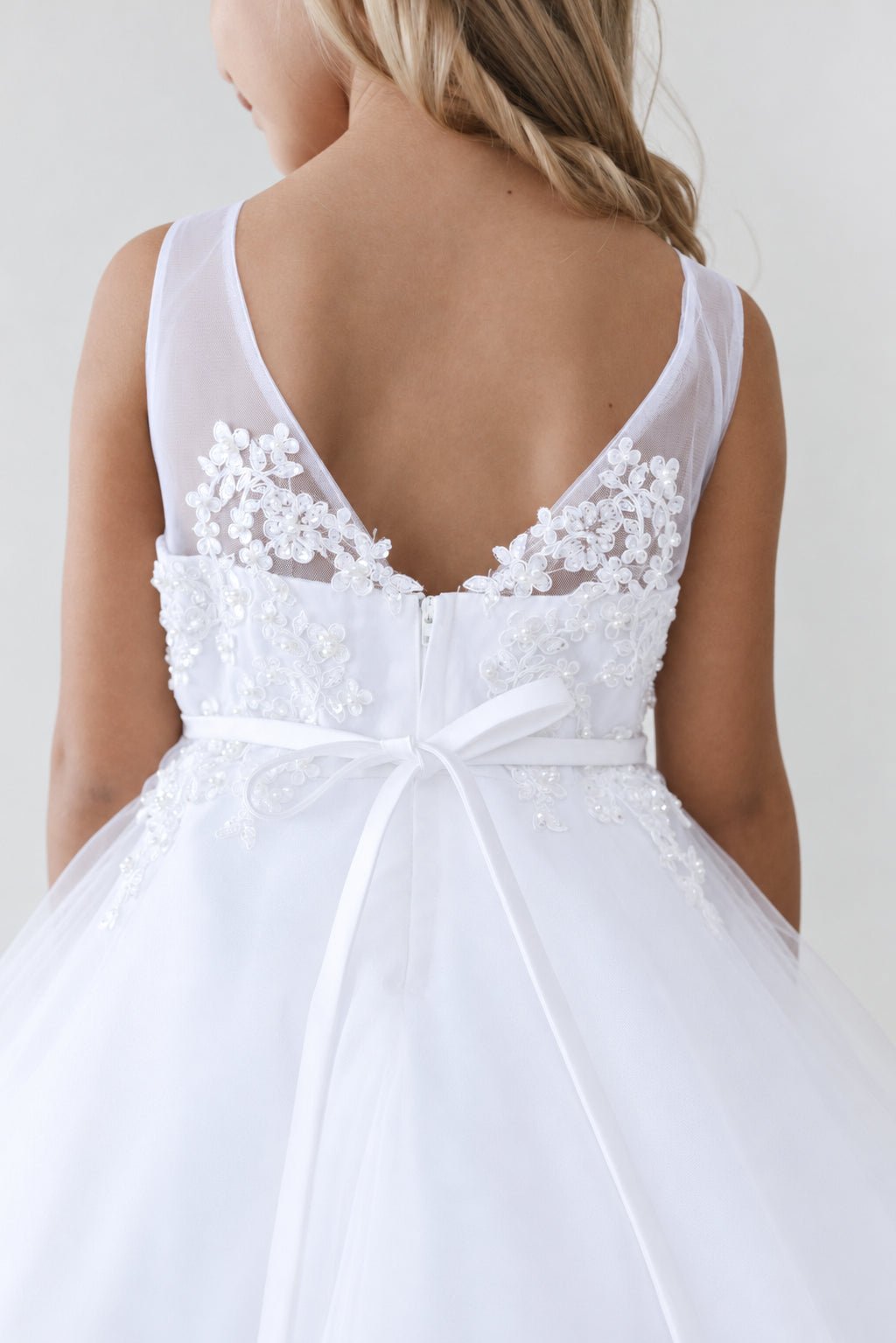 Framed in floral lace, the white flower girl dress has a sheer V back.