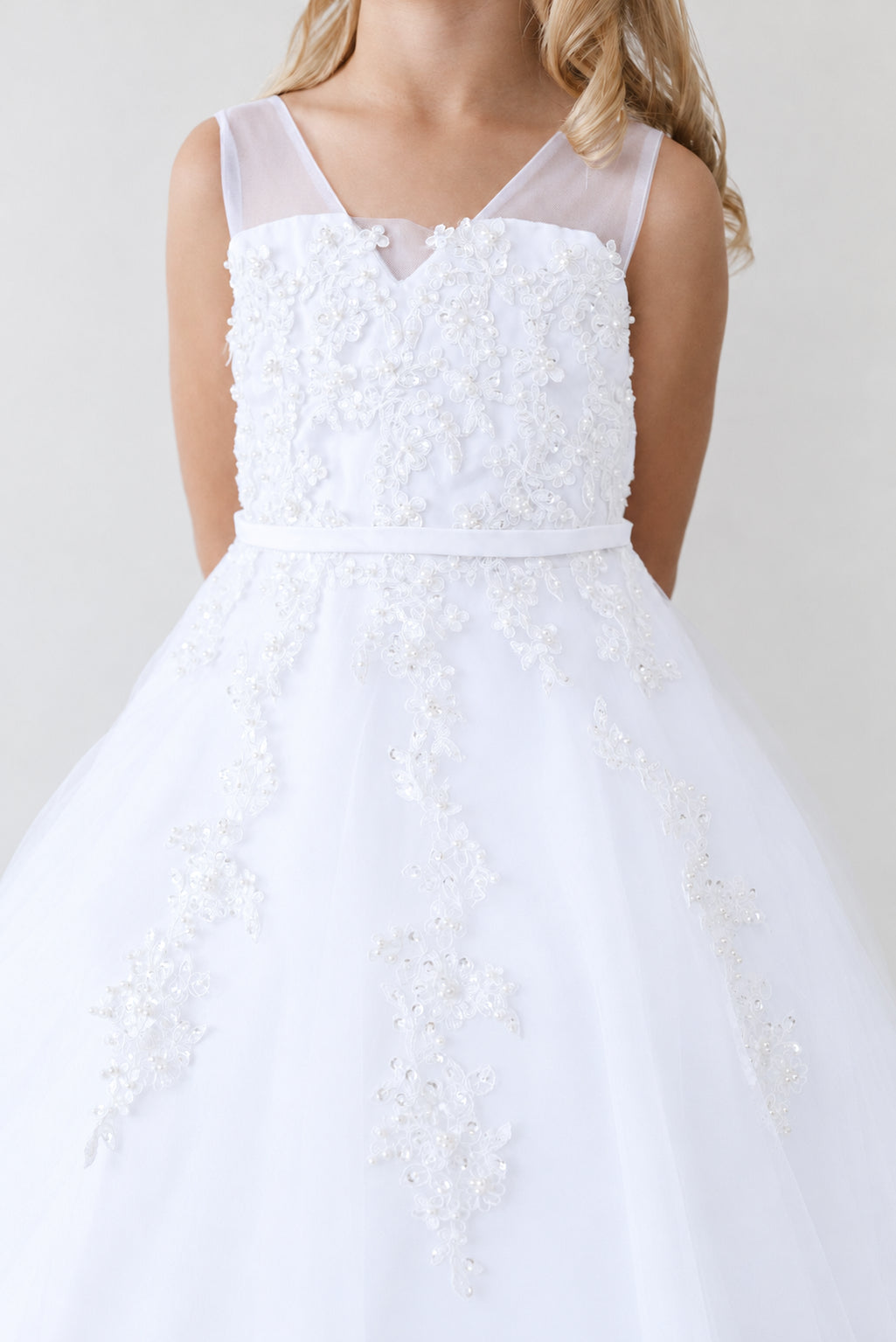 Above the waist, a white flower girl dress has a sheer V neckline.