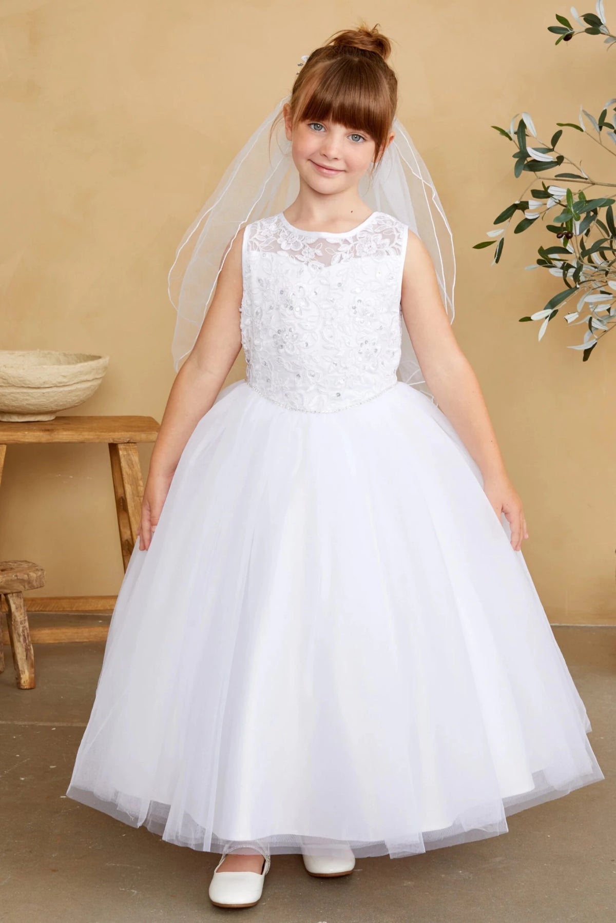 This white flower girl dress displays a flared tulle hem.