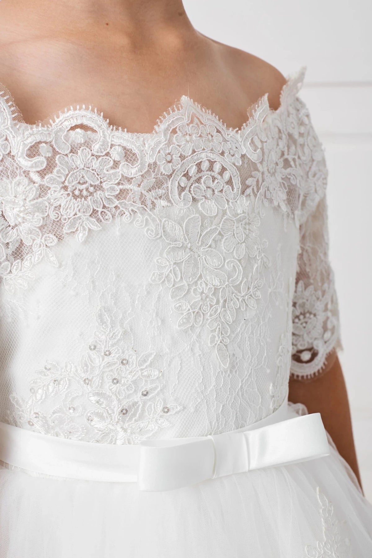 Pearls dot the off-white flower girl dress's scalloped lace neckline.