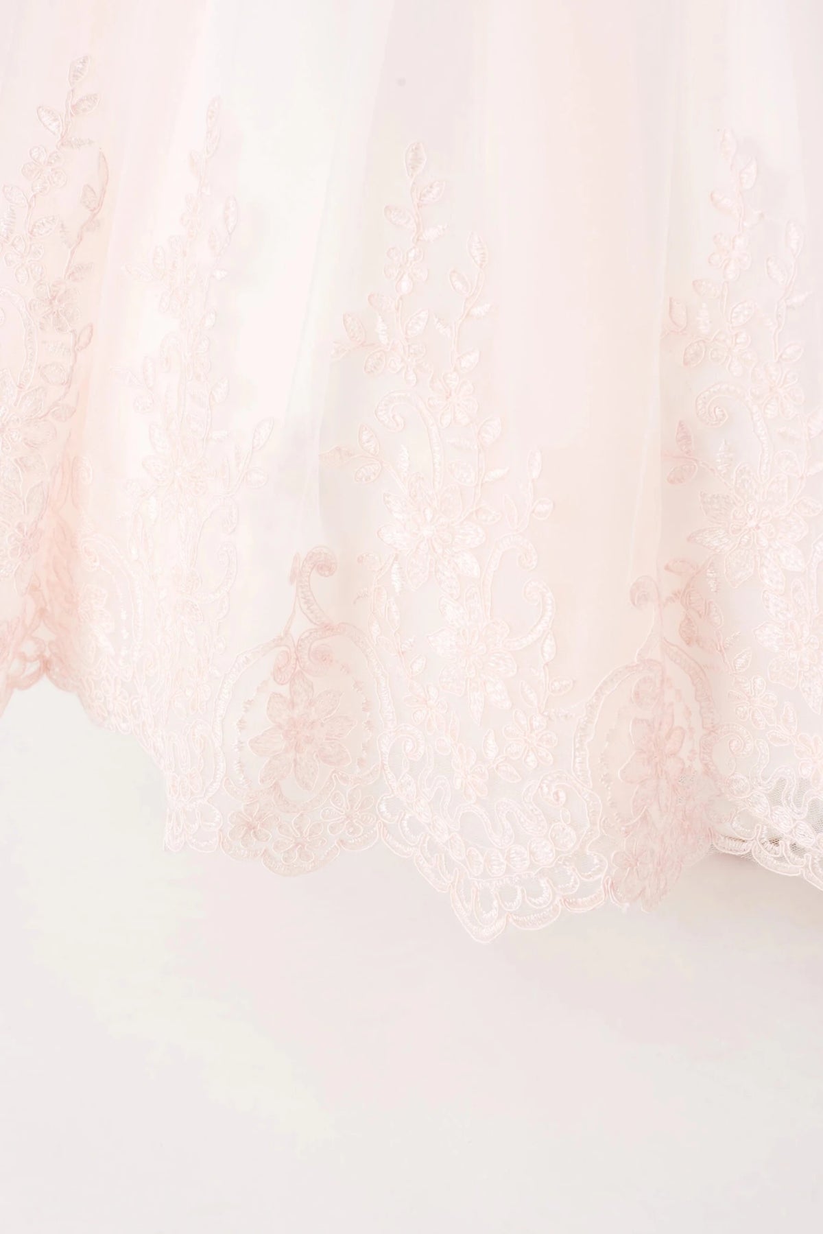 Vine-shaped lace rises from the blush flower girl dress's hem.