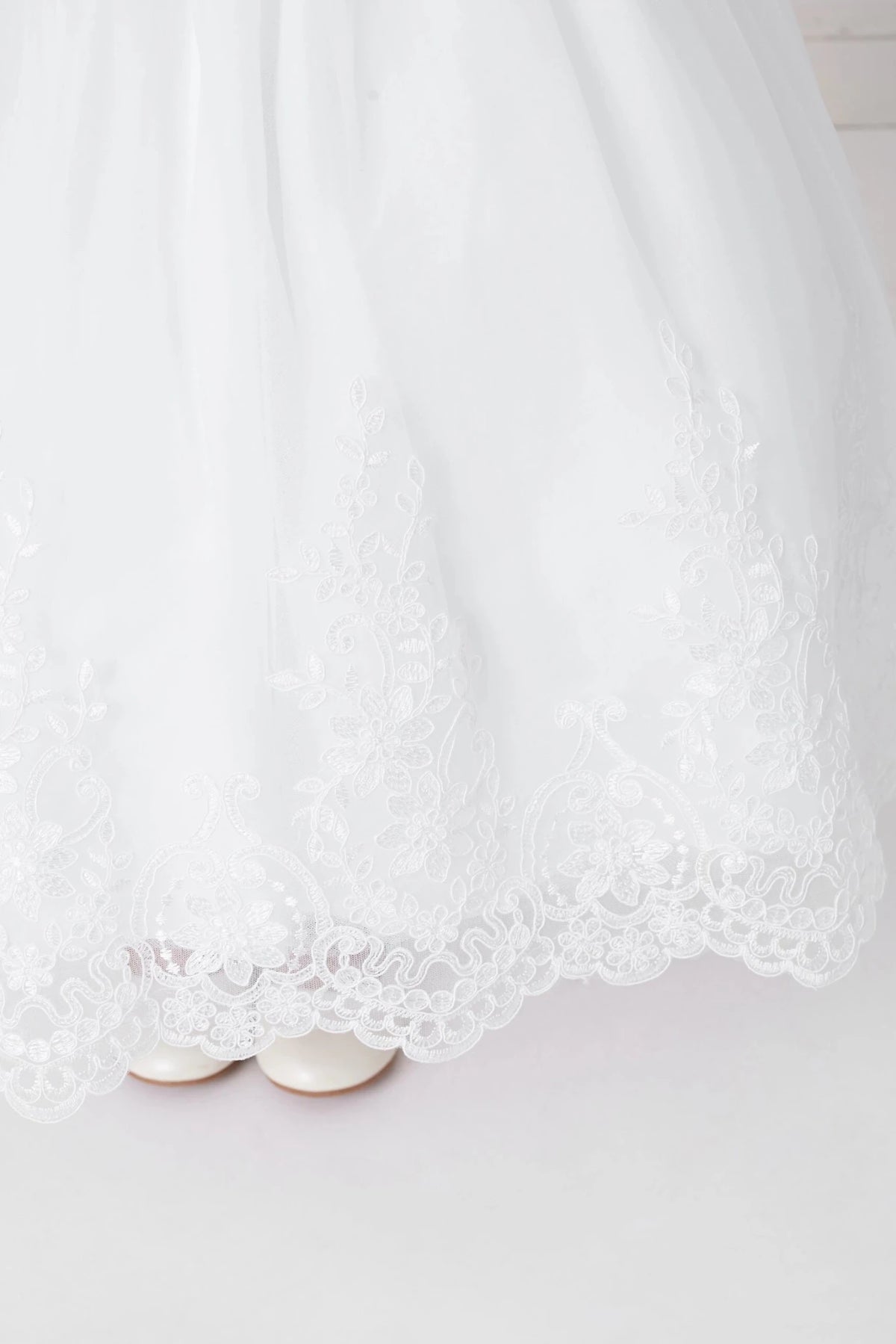 Along the edge, the off-white flower girl dress has leafy lace scallops.