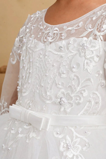 Close-up of a white formal dress with intricate floral lace embroidery, bead embellishments, sheer mesh detailing, and a wide satin waistband bow.