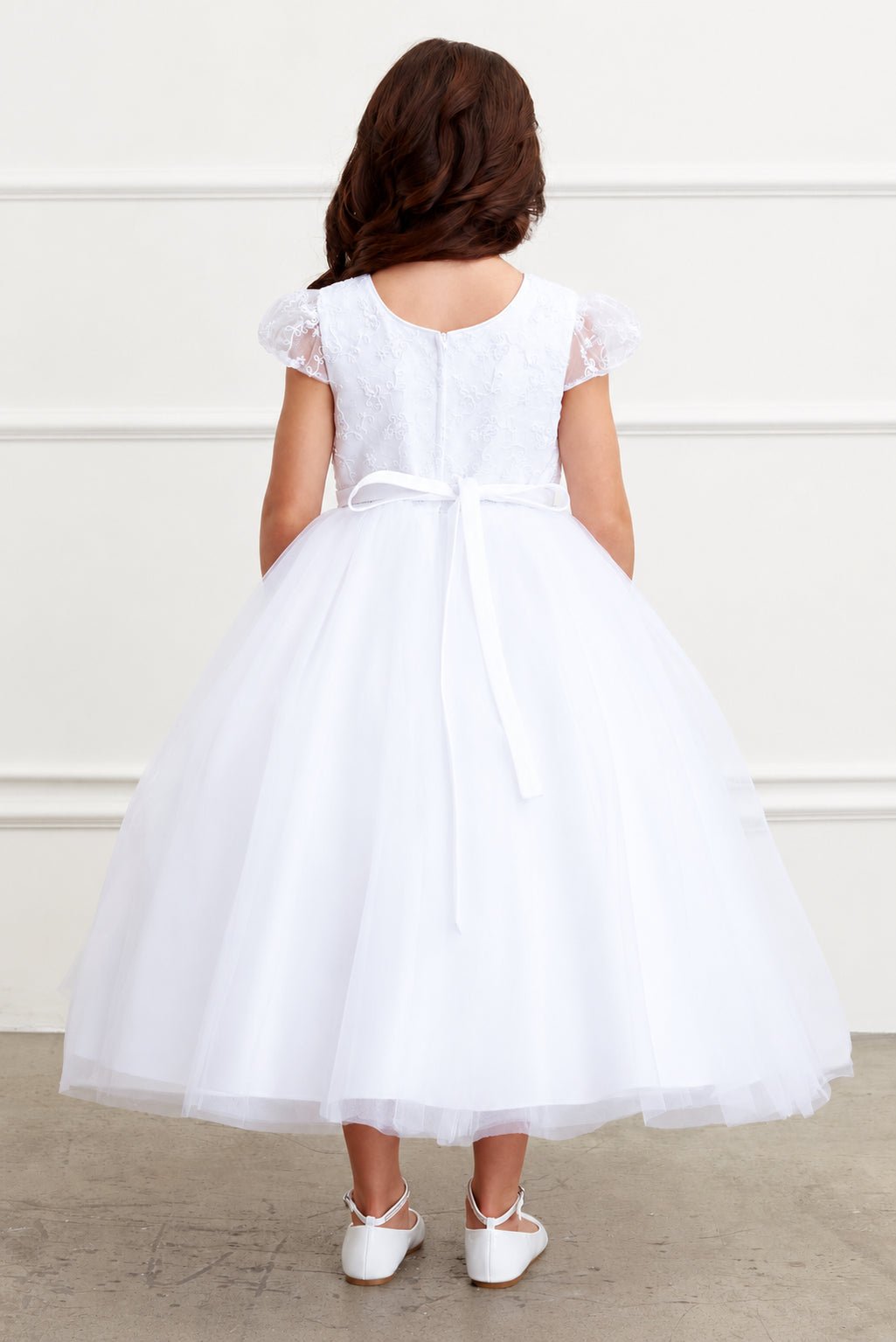 Ribbon tails hang from the white flower girl dress's slim back bow.