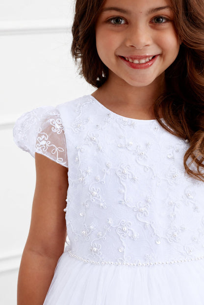 Curling vines and beads texture the white flower girl dress's cap sleeves.