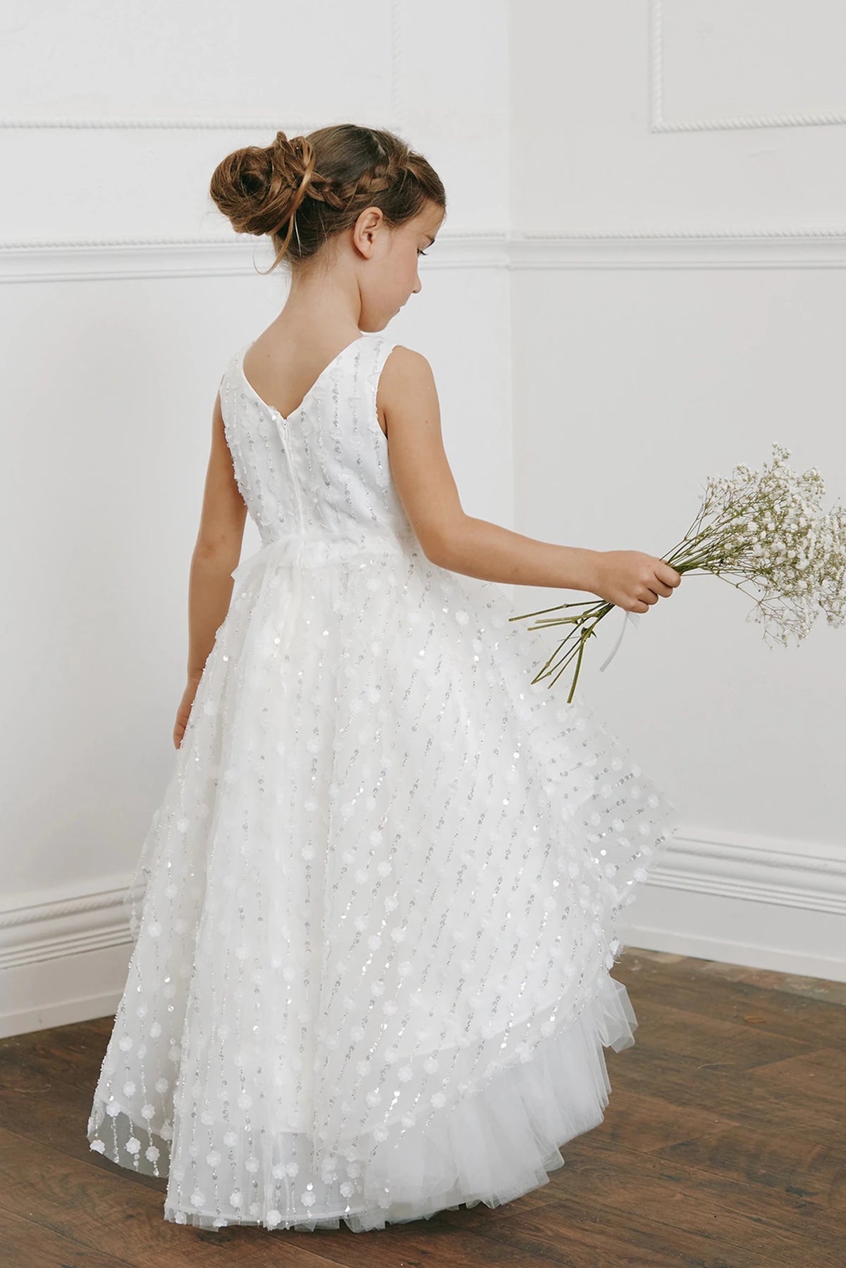 A V back tops the off-white flower girl dress's long, dotted skirt.