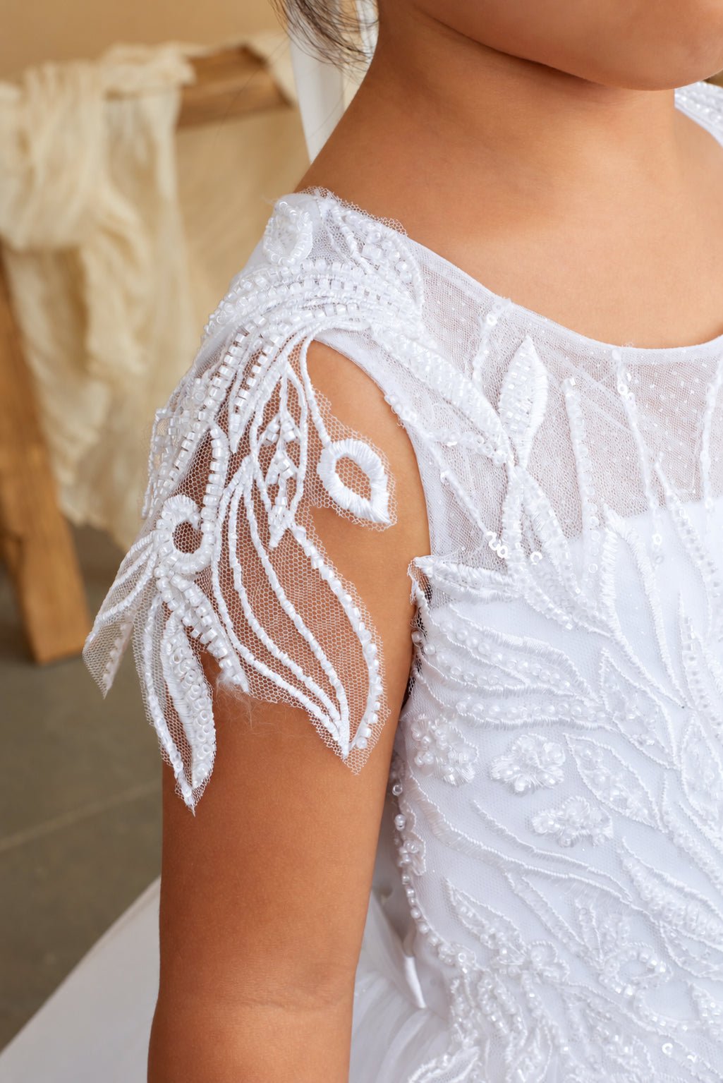 Leaf-shaped beading forms an open cap sleeve on a white flower girl dress.