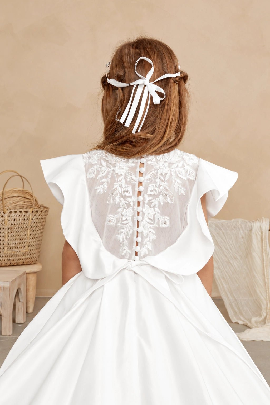 Covered buttons line the off-white flower girl dress's sheer embroidered back.