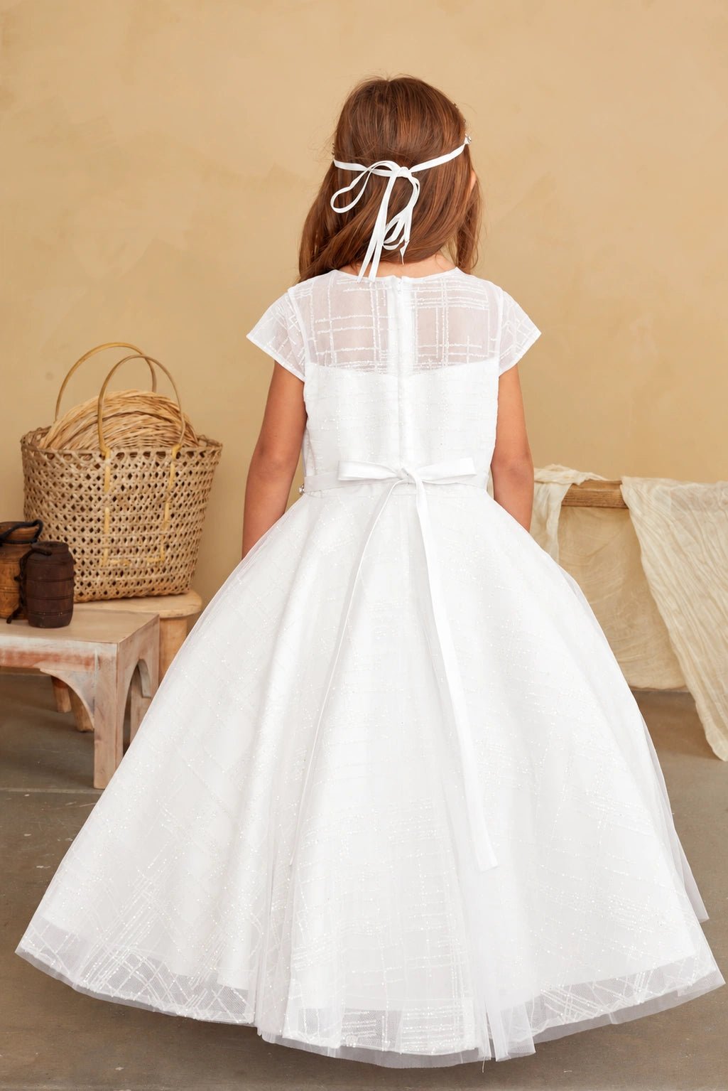 Gridded sheer fabric spans the off-white flower girl dress's upper back.