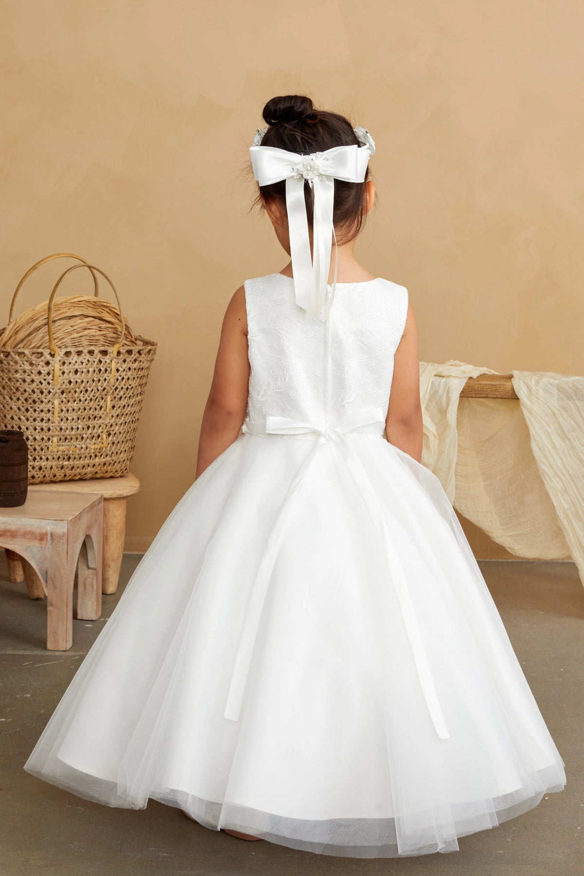 Slender bow tails lie over the off-white flower girl dress's full back skirt.