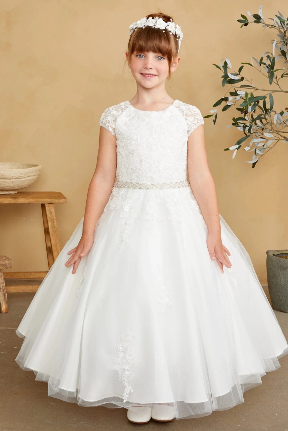 Below the belt, an off-white flower girl dress has lace scattered on tulle.