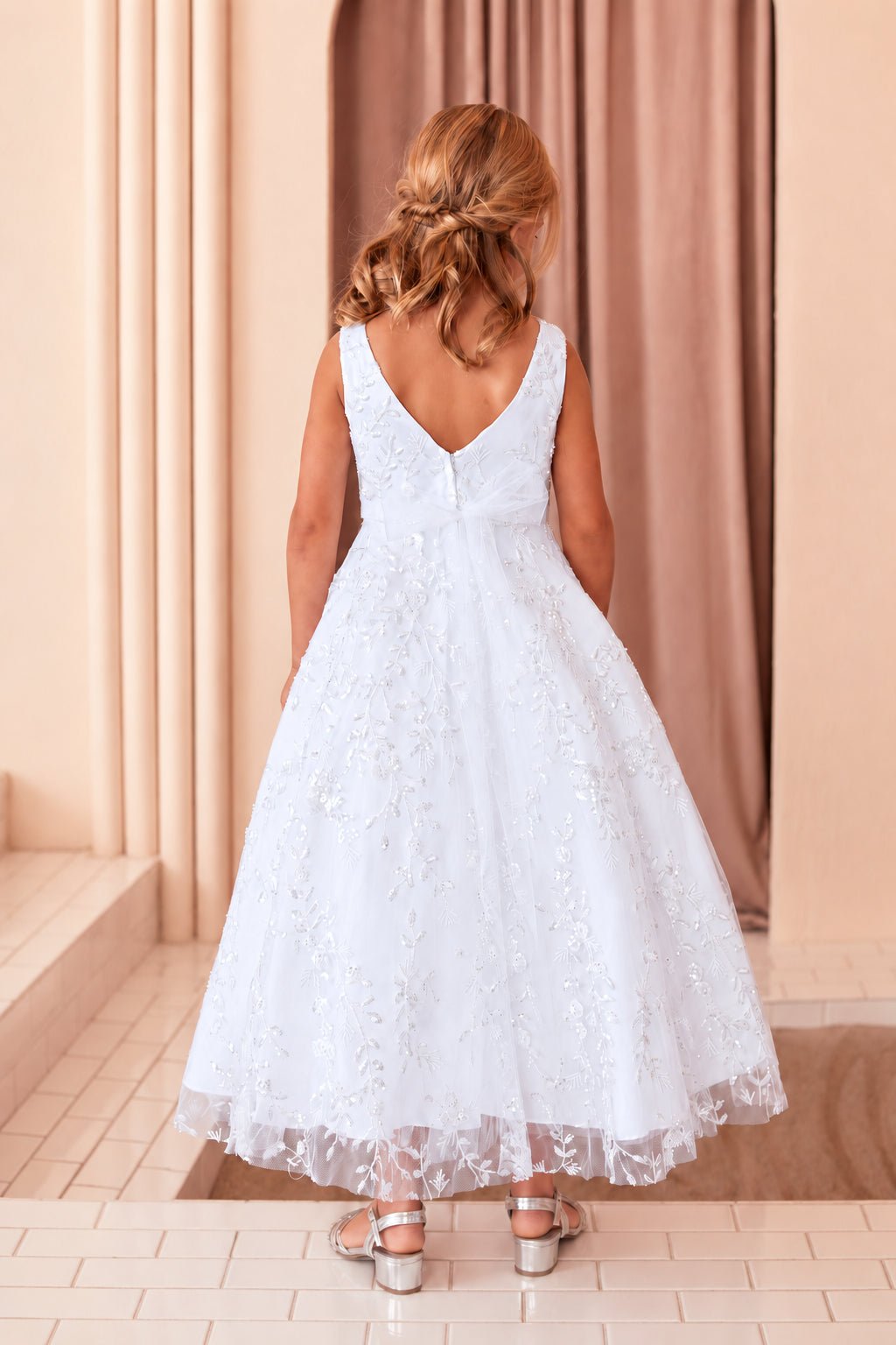 Plunging V back on a white flower girl dress covered in floral lace.