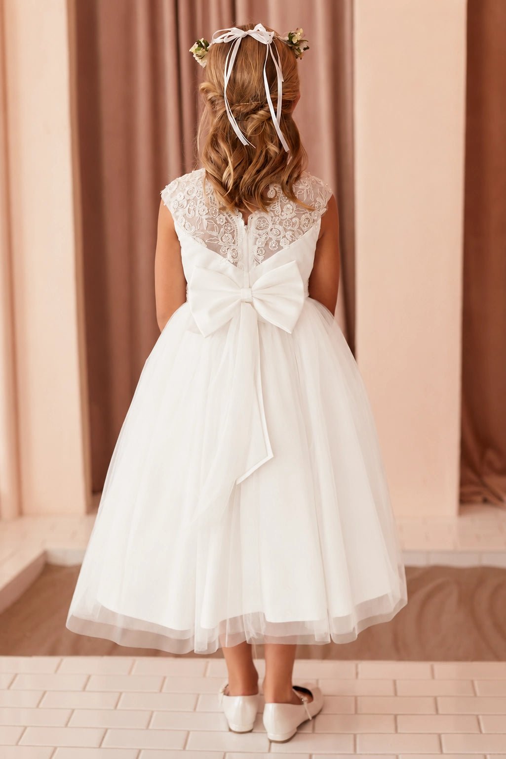 Detailed with an oversized back bow, this off-white flower girl dress.