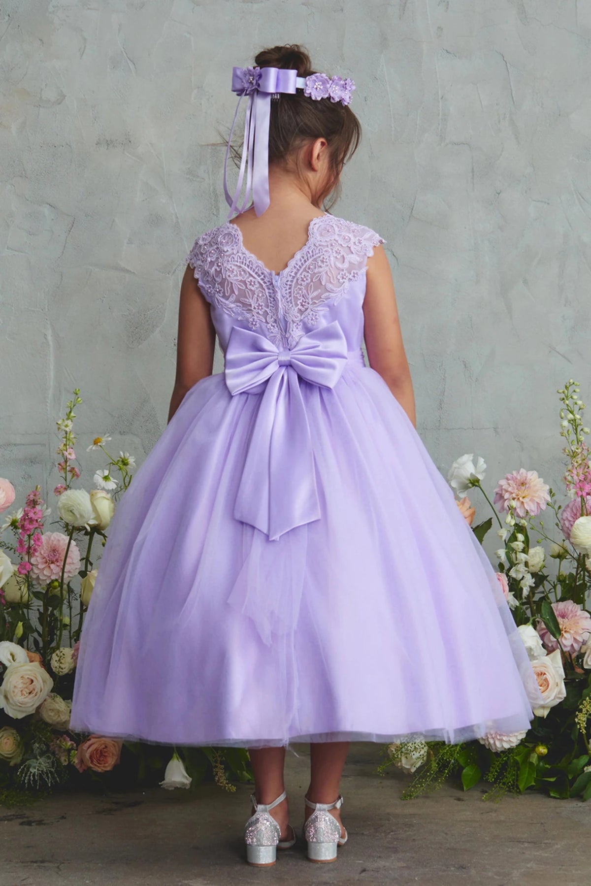 Focus on a large satin back bow of the lilac flower girl dress.
