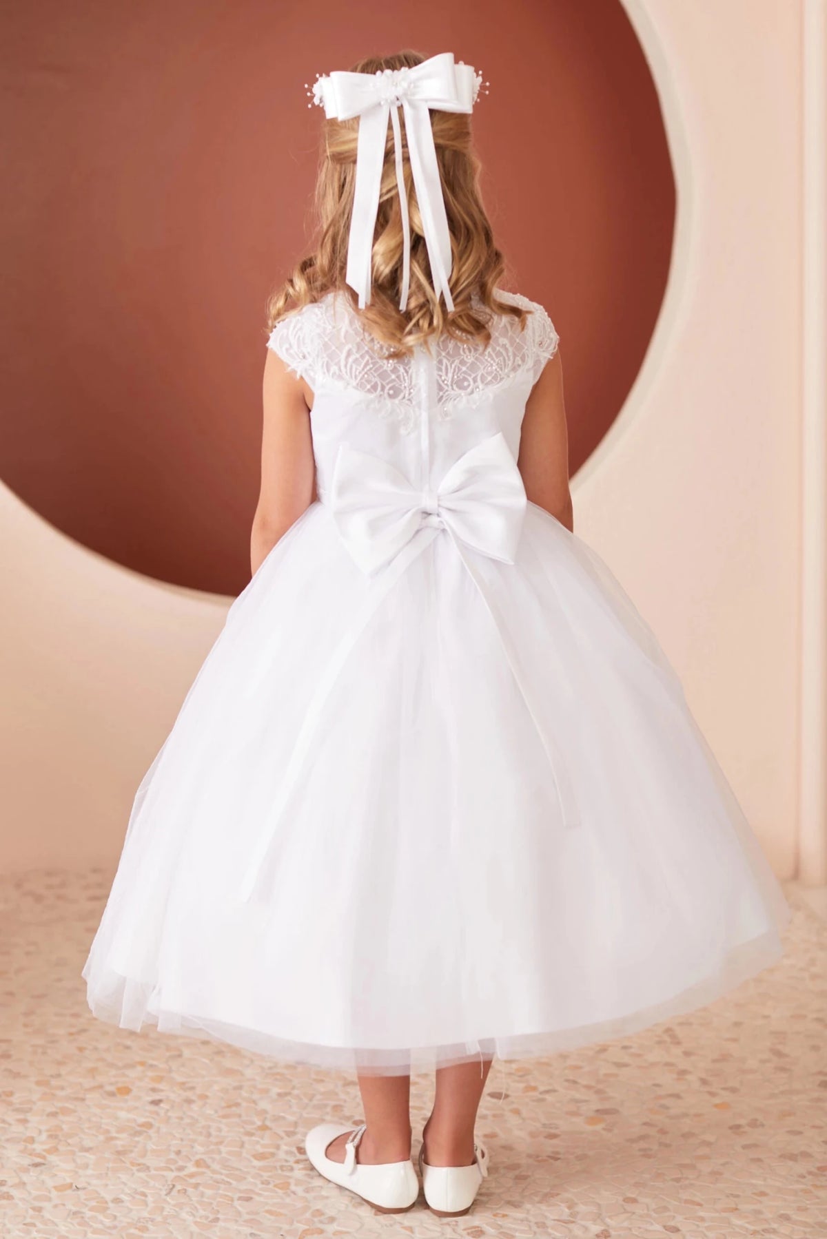 Emphasis on a large satin back bow of the white flower girl dress.