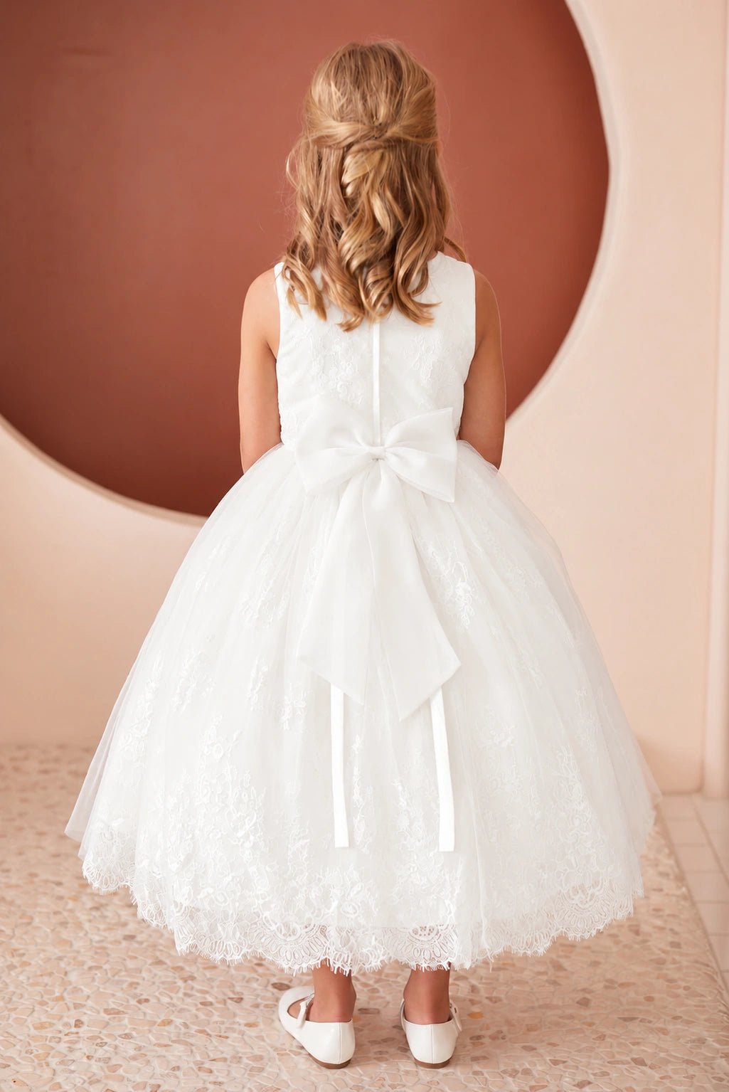 Ribbon tails drape over the off-white flower girl dress's lace back skirt.