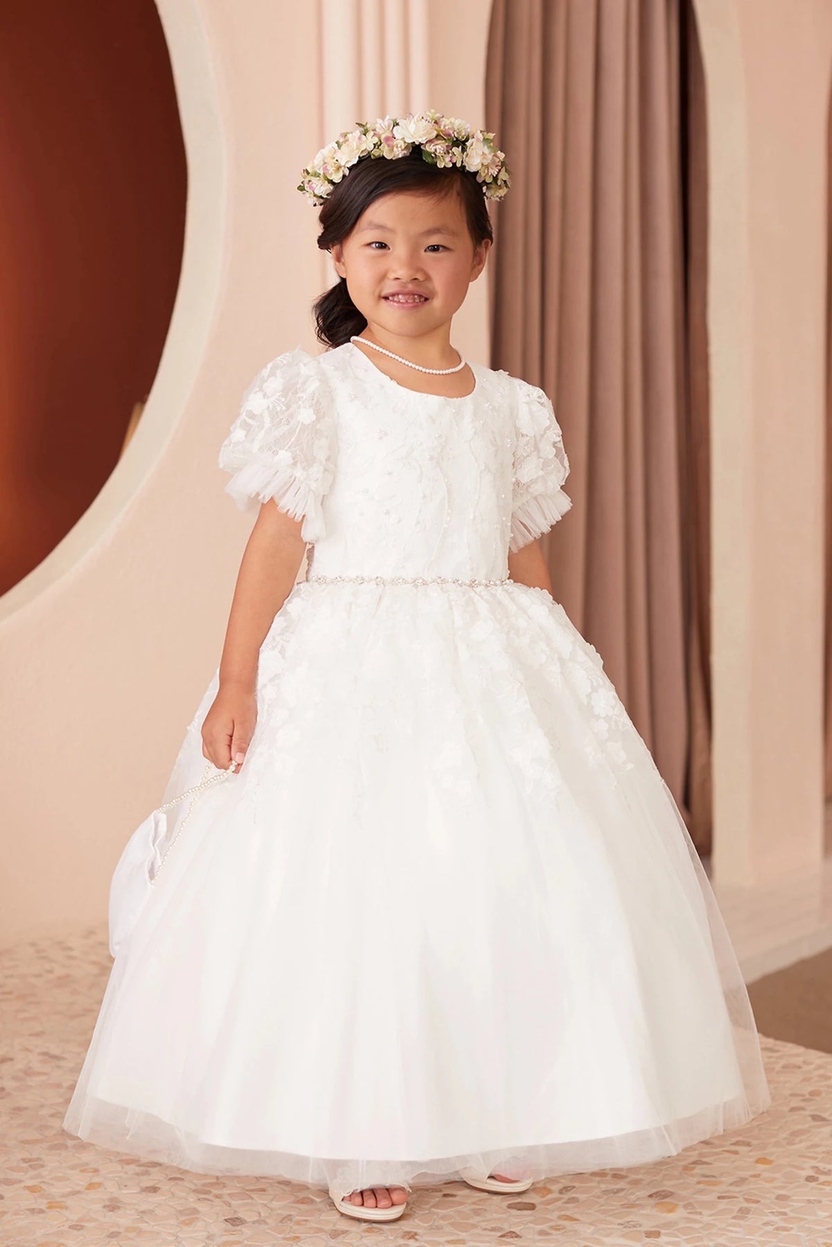 Ruffled sleeve edges accent the off-white flower girl dress's puff shoulders.