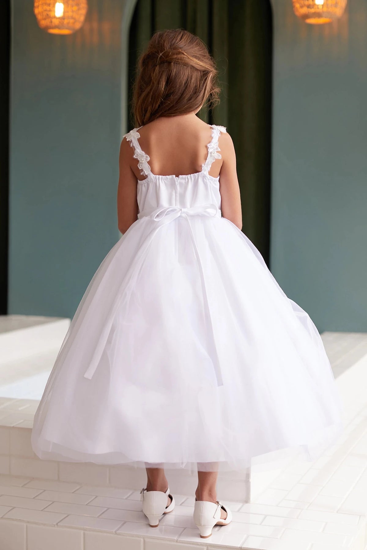The white flower girl dress features flower-trimmed shoulder straps.