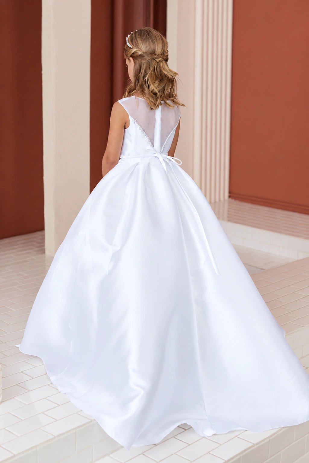An oversized bow crowns the white flower girl dress's sweeping satin train.