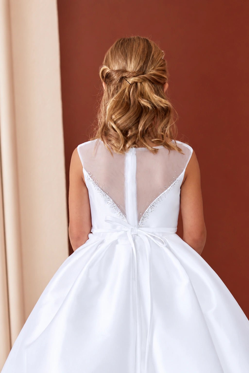 Transparent mesh forms the white flower girl dress's deep V back.
