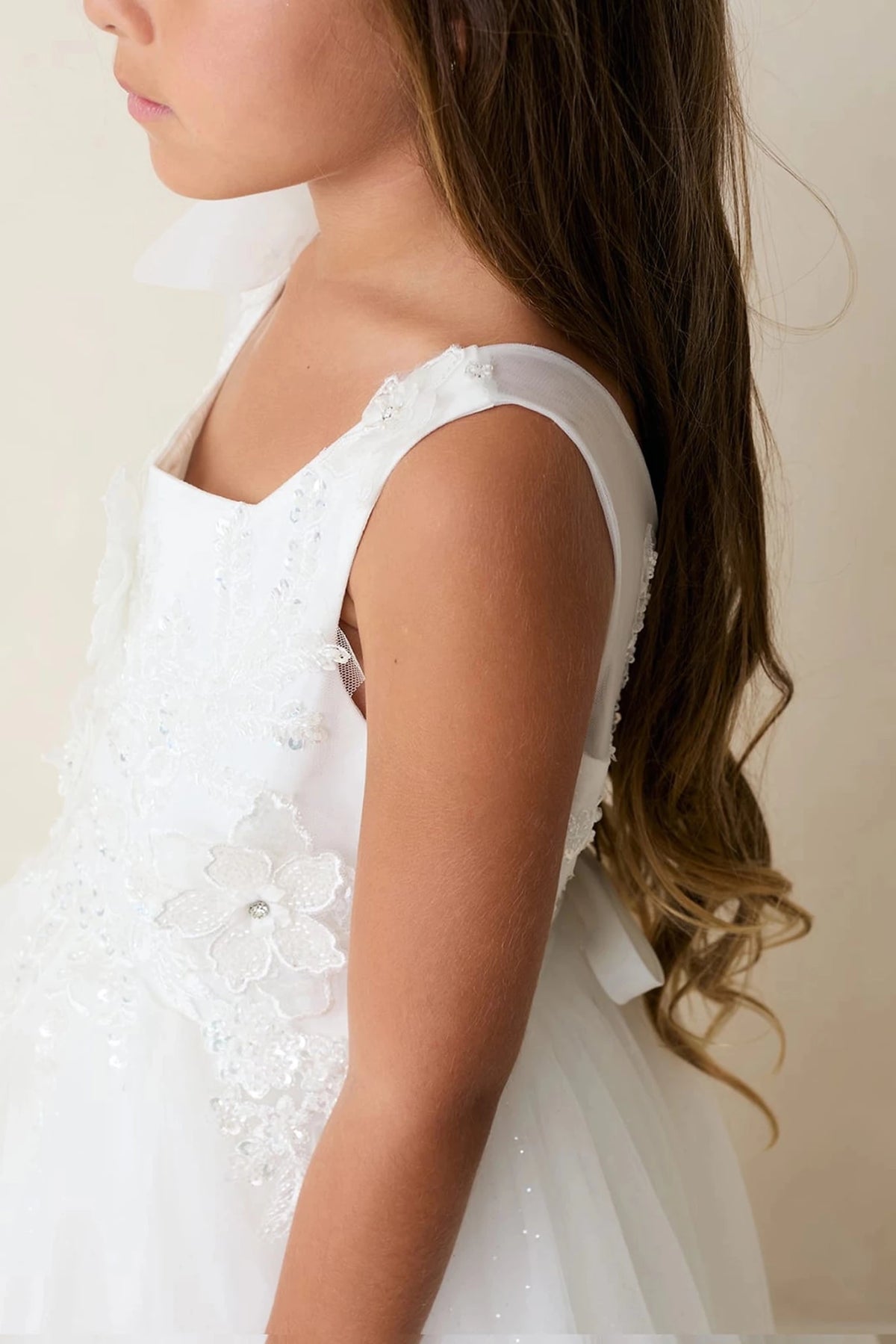 Highlighting a floral shoulder strap on an off-white flower girl dress.