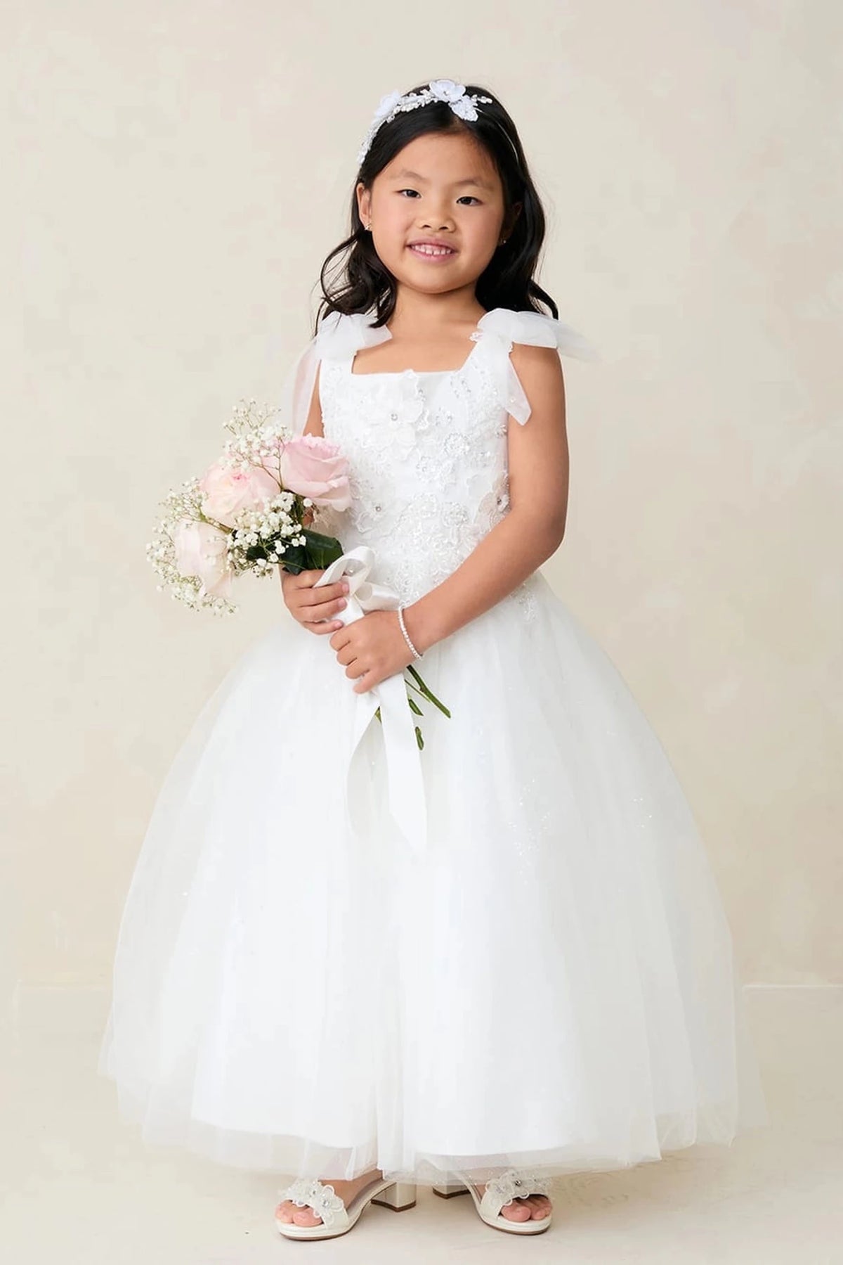 The off-white flower girl dress features shoulder ribbon bows.