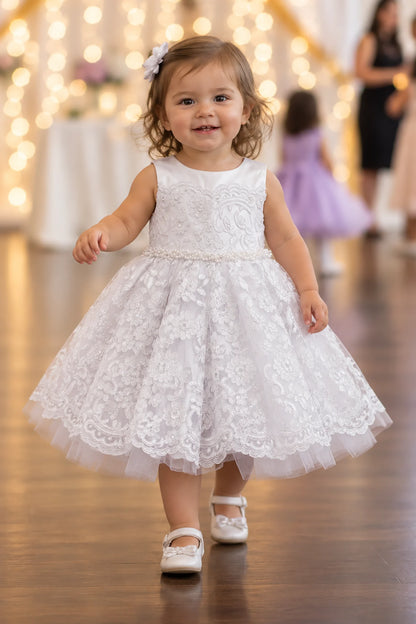 White flower girl dress with a pearl waistband and scalloped lace skirt.