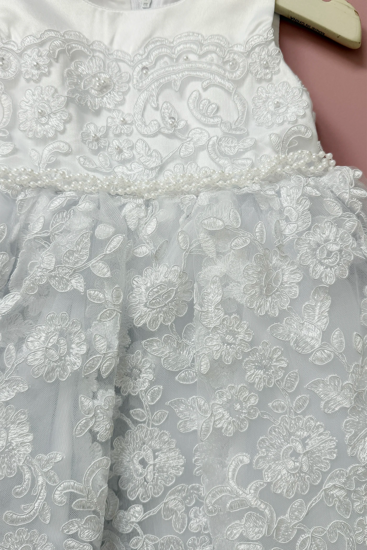 Braided pearls border the waist of the white flower girl dress above floral lace.
